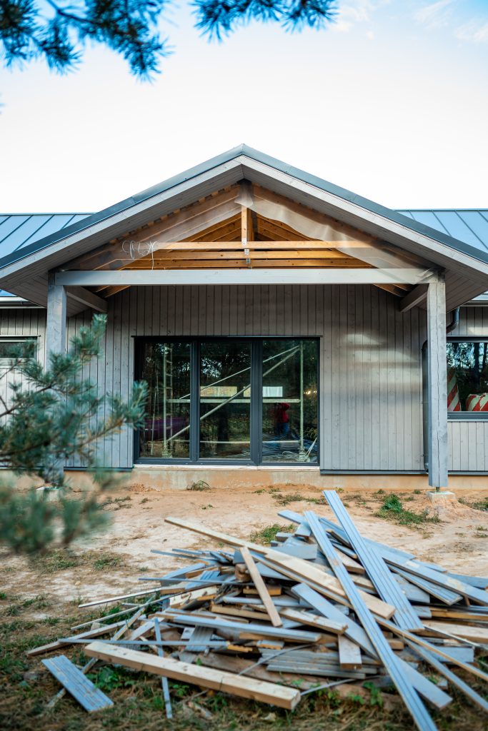 Maison en bois moderne en construction avec revêtement bleu et charpente exposée sous un ciel ensoleillé