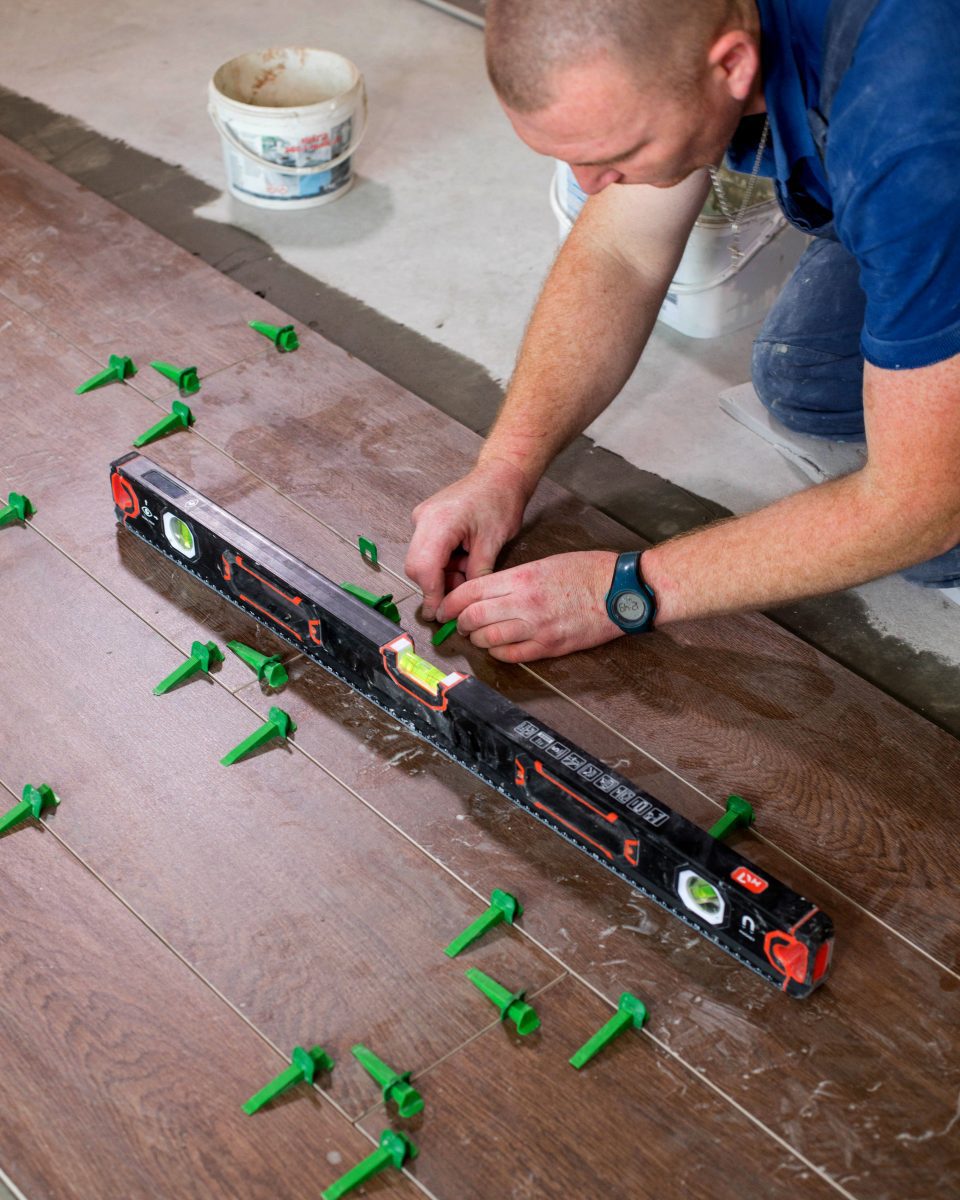 Tuiler posant des clips dans un système de nivellement de carreaux sur le sol d'une nouvelle maison.