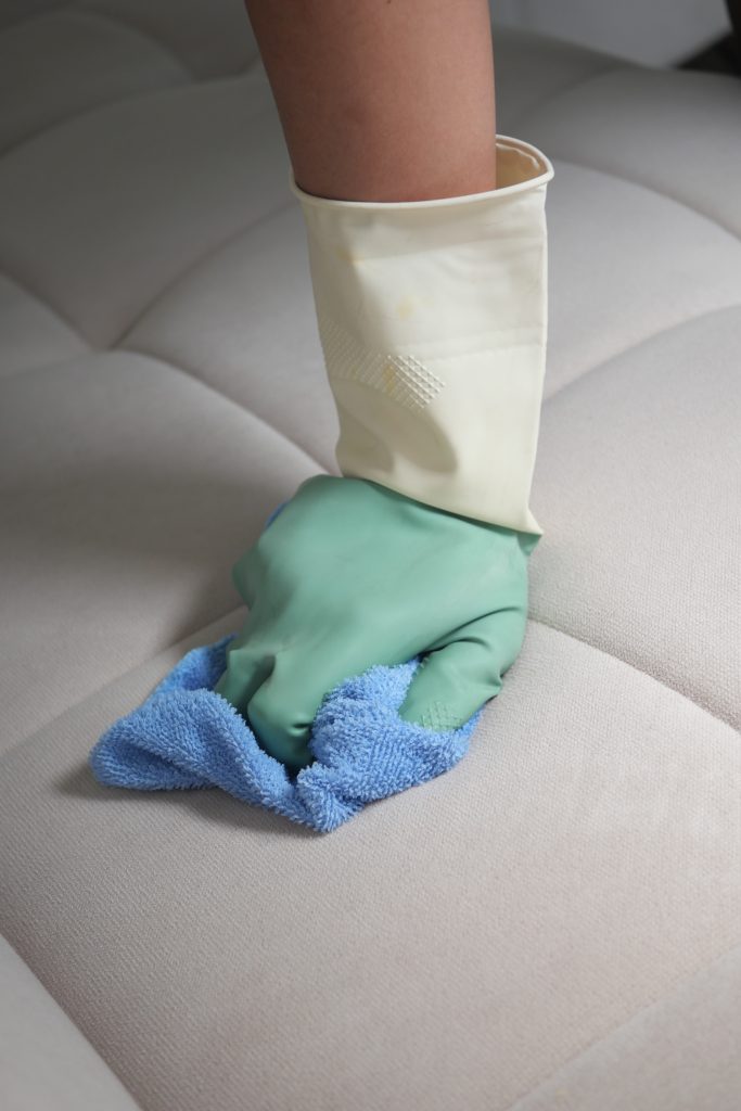 Femme nettoyant un canapé avec un chiffon et des gants dans un salon confortable