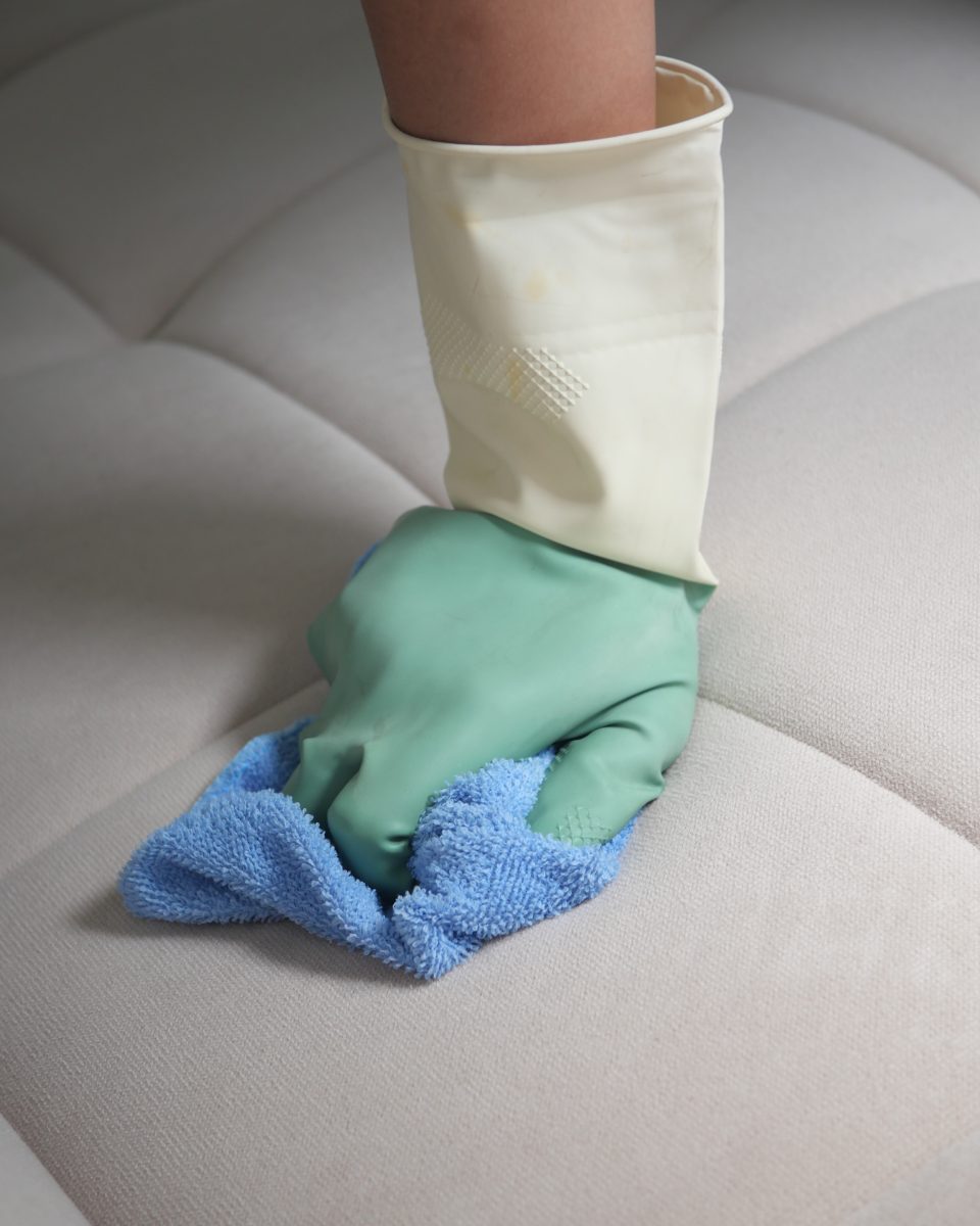 Femme nettoyant un canapé avec un chiffon et des gants dans un salon confortable