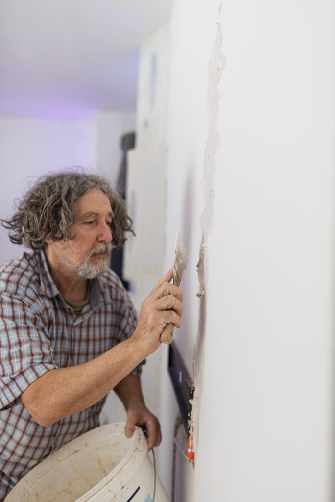 Un ouvrier en train d'enduire un mur à l'intérieur, montrant la technique d'application du plâtre.