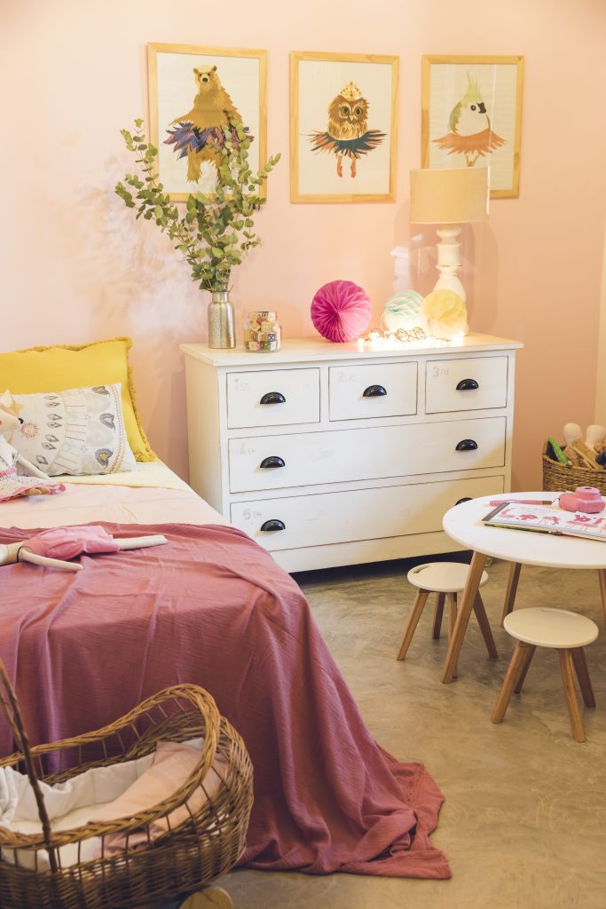 Chambre de fille avec des couleurs roses, une poussette de jouet et une table de dessin