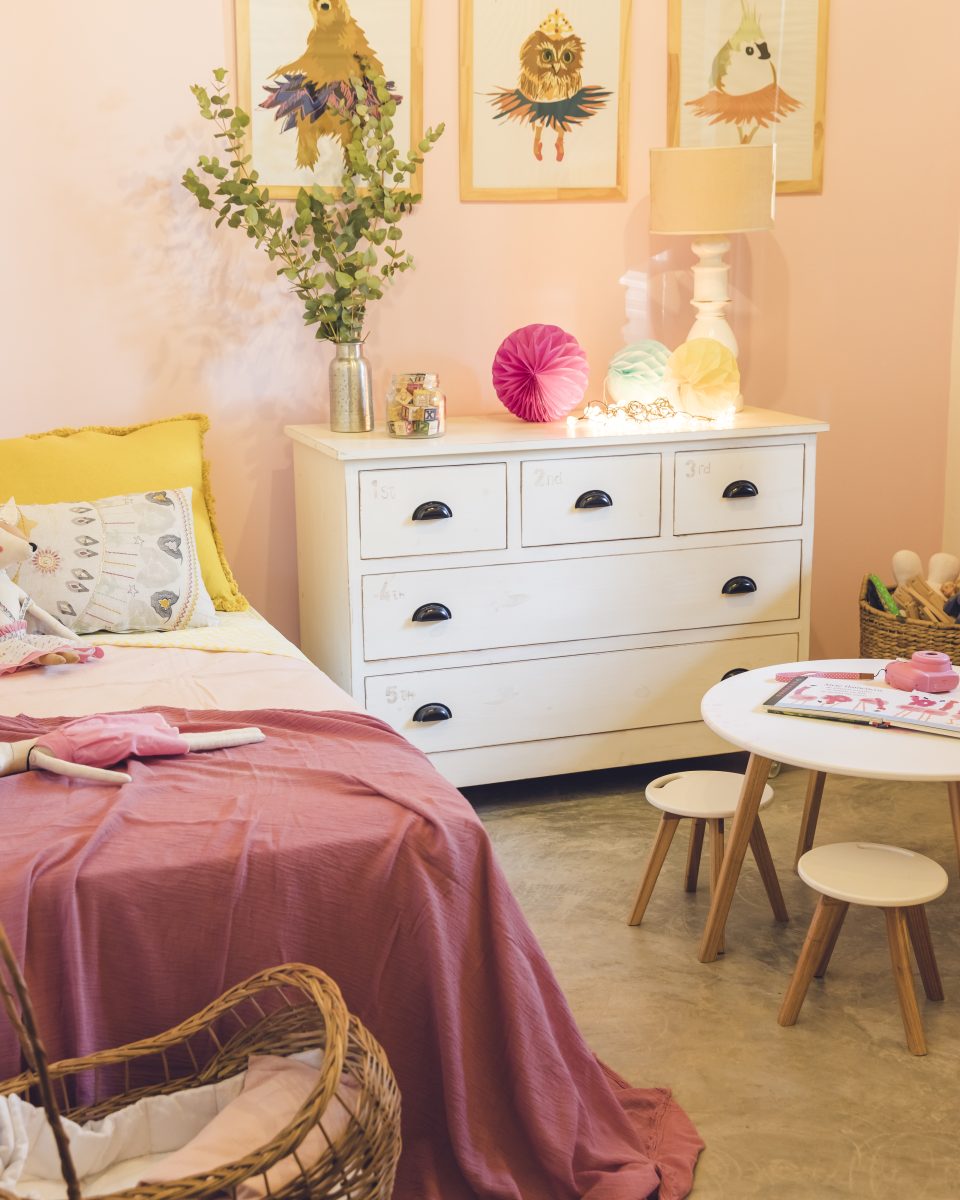 Chambre de fille avec des couleurs roses, une poussette de jouet et une table de dessin